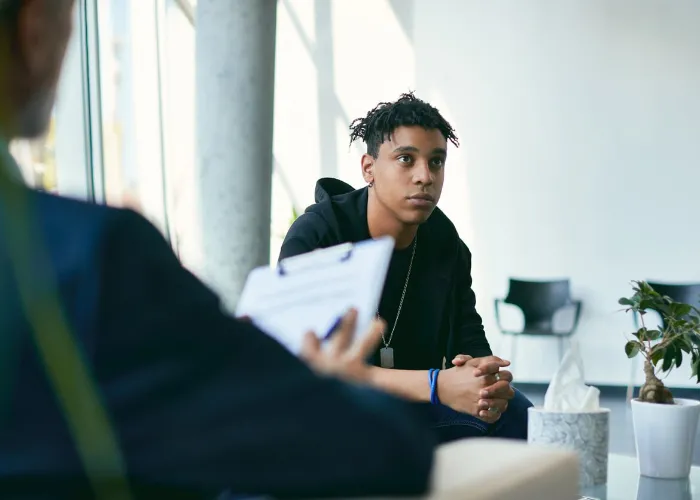 Black teenage boy having counselling with mental health professional during therapy session.