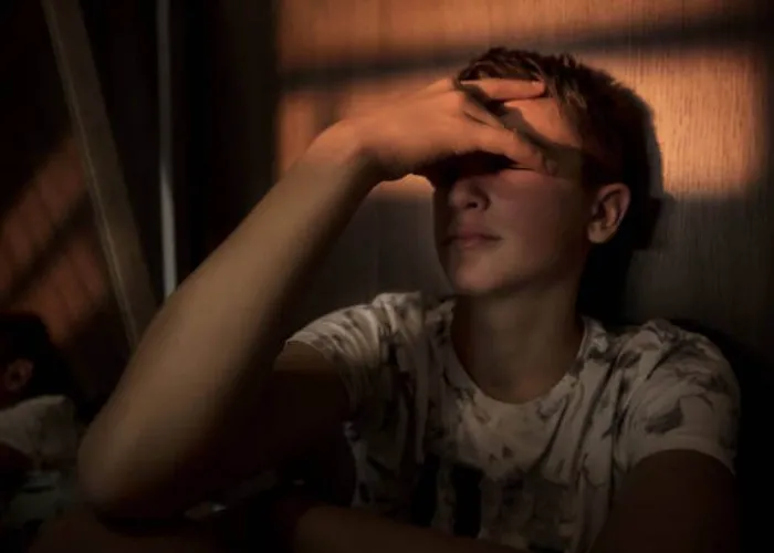 portrait of a teenager boy sitting in the dark room, with a beam of light over his eyes