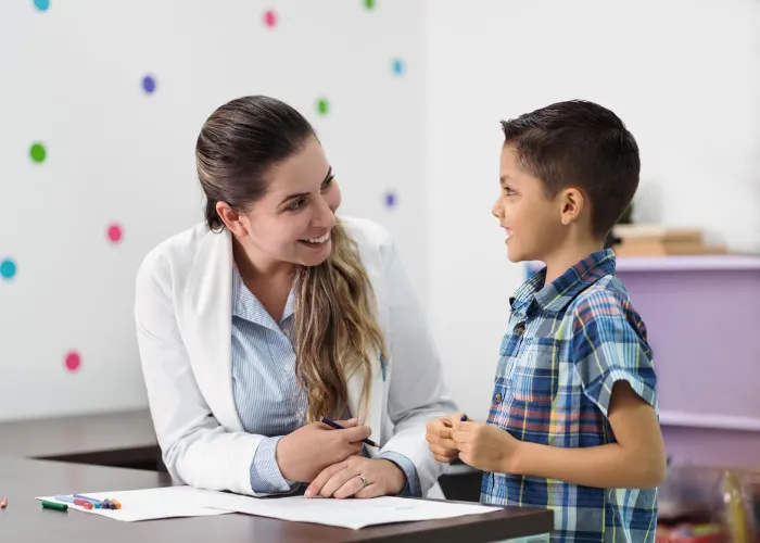 A happy latin female psychologist and a little boy smiling at each other in her office.